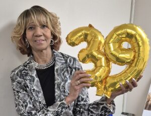 Sandra smiling and holding up balloons celebrating her 39 years at Magdala House