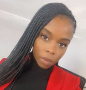 Portrait of Tiffiani Mitchell, a Black woman with long braided hair, wearing a red blazer and black turtleneck, seated and facing the camera with a calm, confident expression.