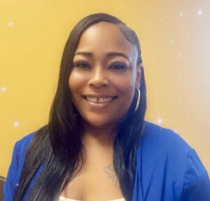 Smiling woman in a blue blazer standing in front of a yellow background.